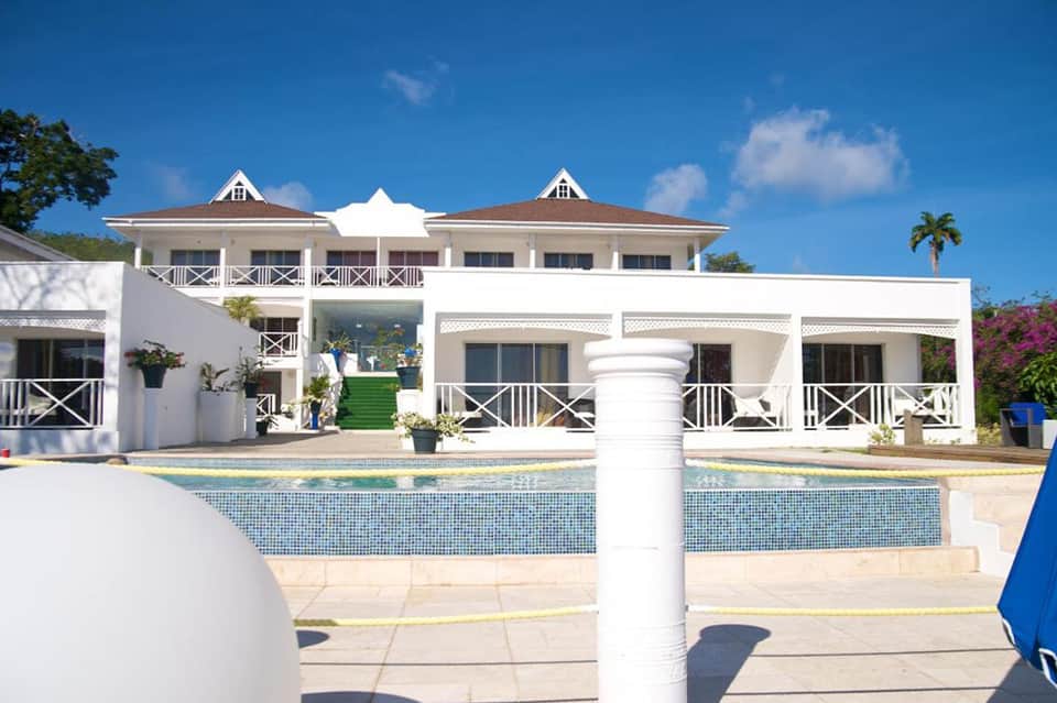 White luxury home with columned porch and blue-tiled pool overlooking palm trees