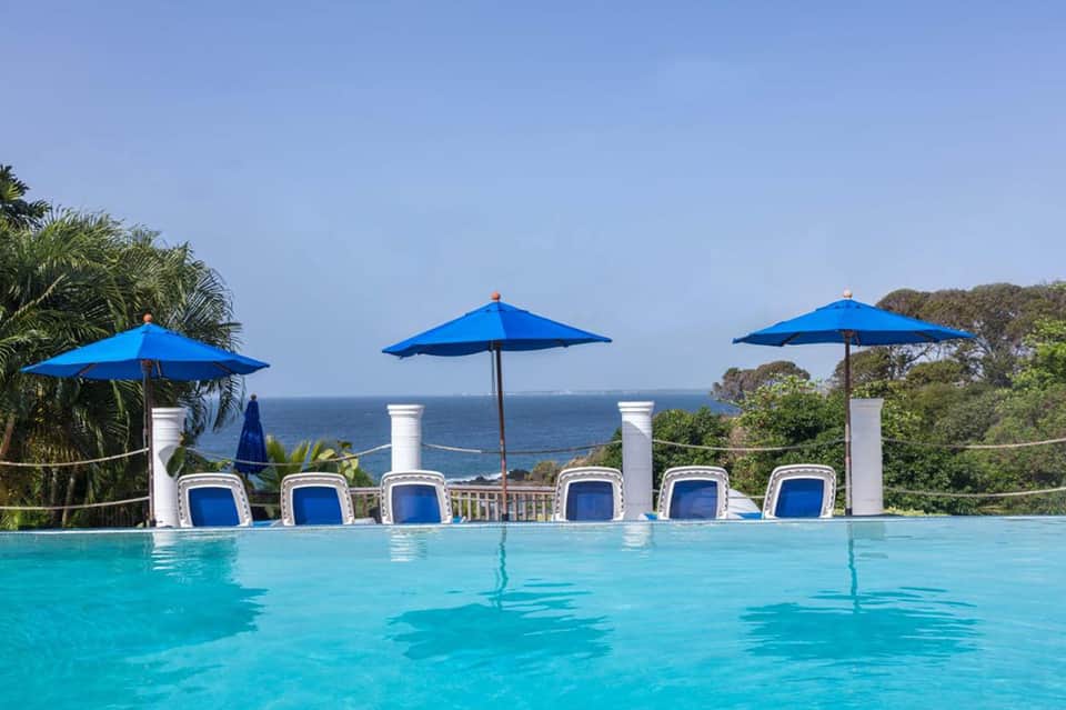 Infinity pool with blue umbrellas and lounge chairs overlooking ocean cliff vista
