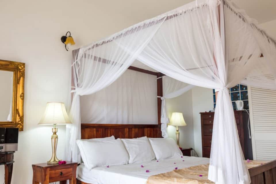 Elegant bedroom with wooden four-poster canopy bed draped in white curtains and traditional furnishings