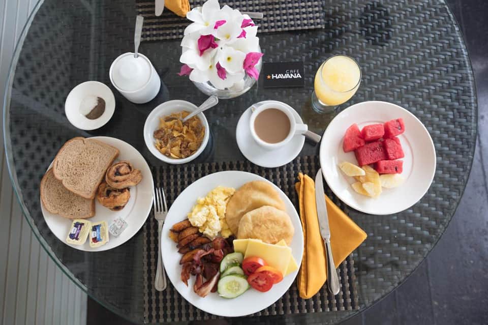 Breakfast spread on table including eggs, bacon, fruit, bread, coffee, and fresh flowers