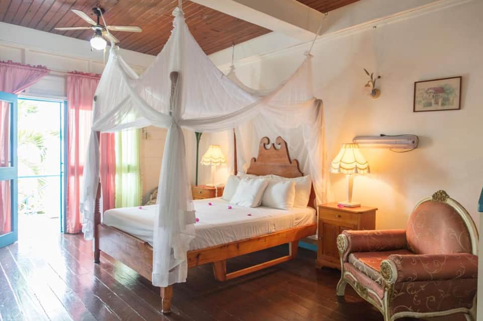 Luxury bedroom with white canopy bed, wooden furniture, warm lighting, and tropical door view