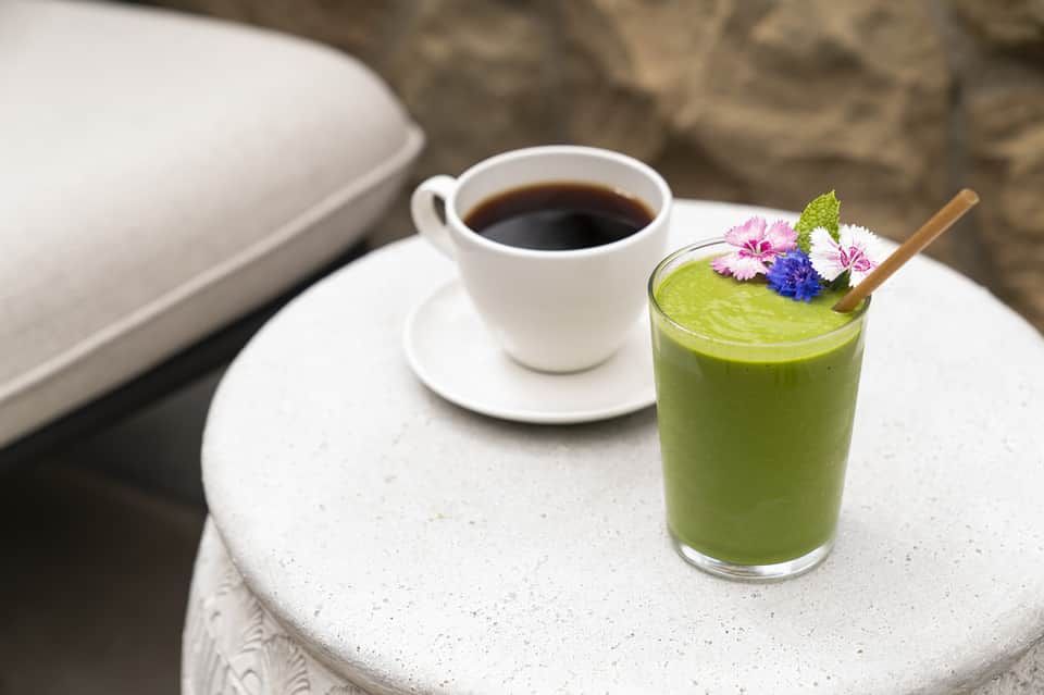 White coffee cup and green smoothie with edible flowers on concrete table outdoors