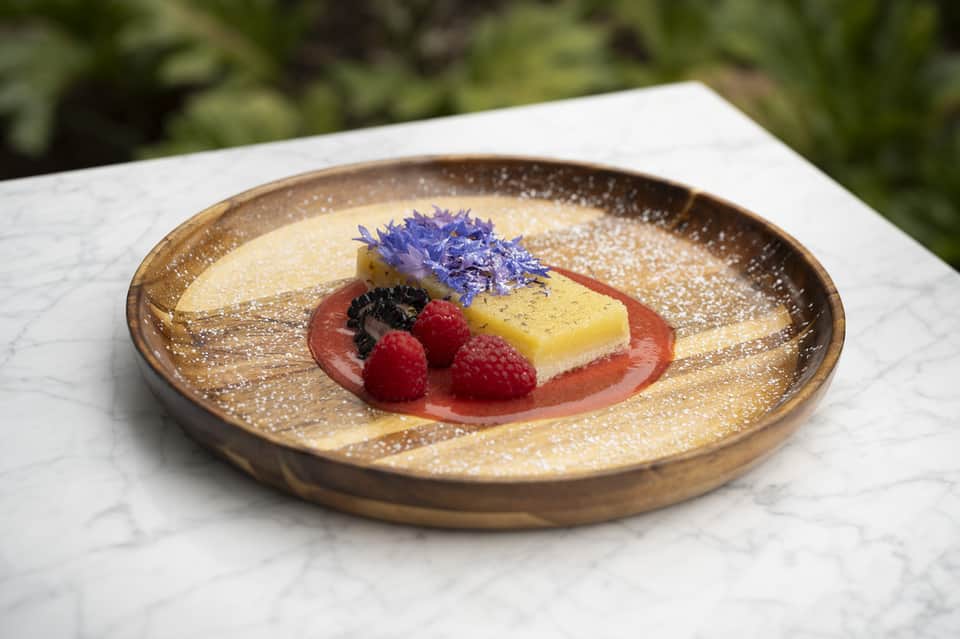 Gourmet dessert plated on a bronze dish with berries and edible flowers