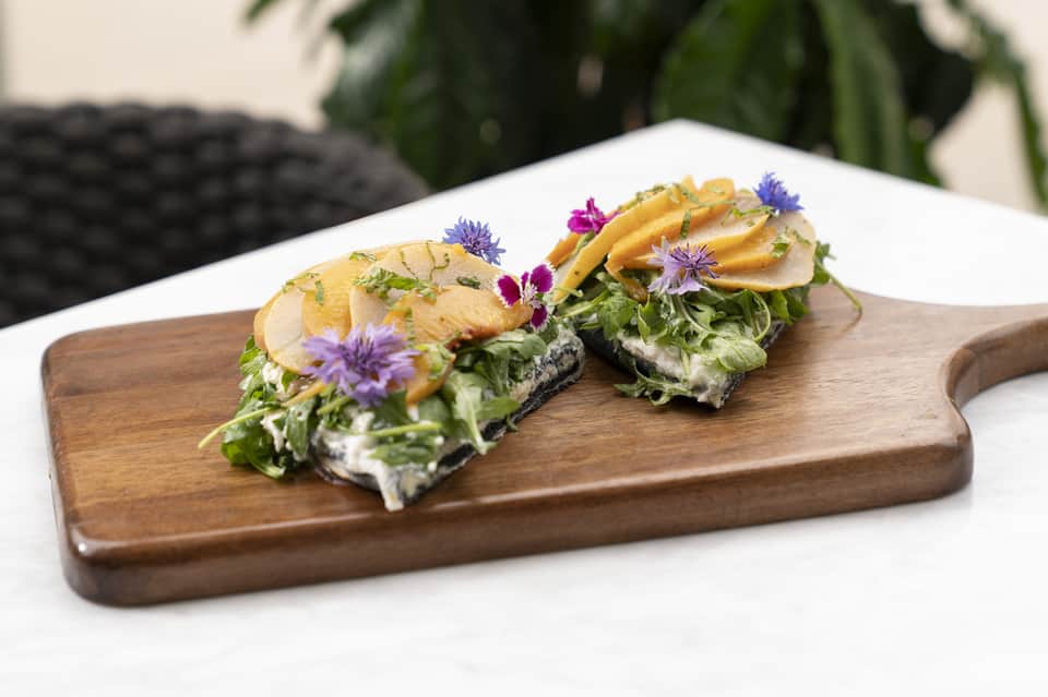 Plated appetizer with decorated toast, greens, and edible flowers on wood board