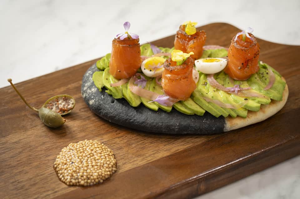 Gourmet appetizer plate with avocado spread, prawns, and edible flowers on wooden board