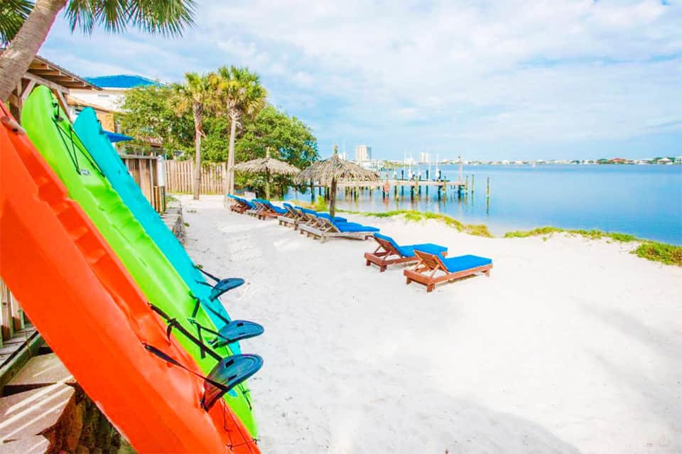 Beach resort with colorful kayaks on white sand, palm trees, lounge chairs, and bay view