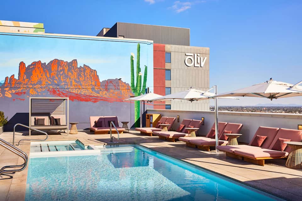 Rooftop pool deck with loungers, umbrellas, and desert mountain mural on modern hotel