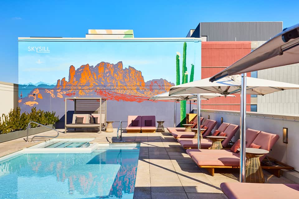 Rooftop pool with desert mural, lounge chairs, umbrellas, and contemporary architectural design