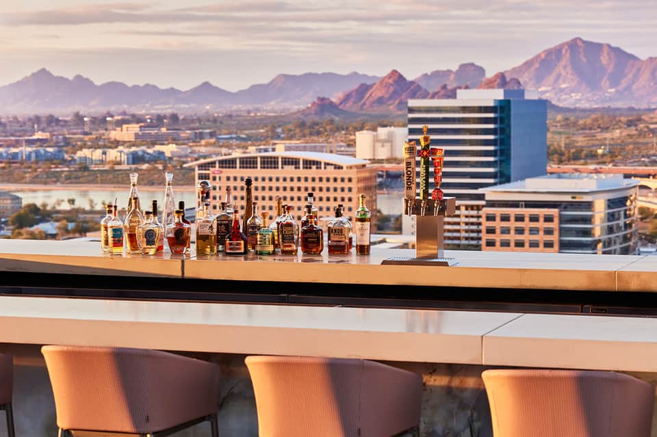 Rooftop bar with liquor bottles and city skyline with mountains backdrop