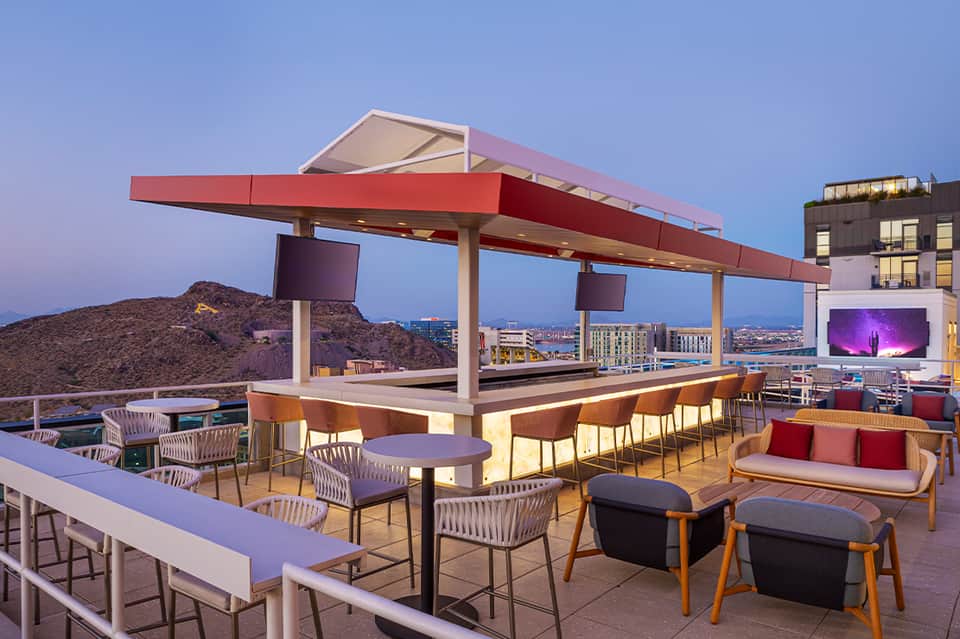 Modern rooftop bar with illuminated canopy, city skyline views, lounge seating, and evening ambiance