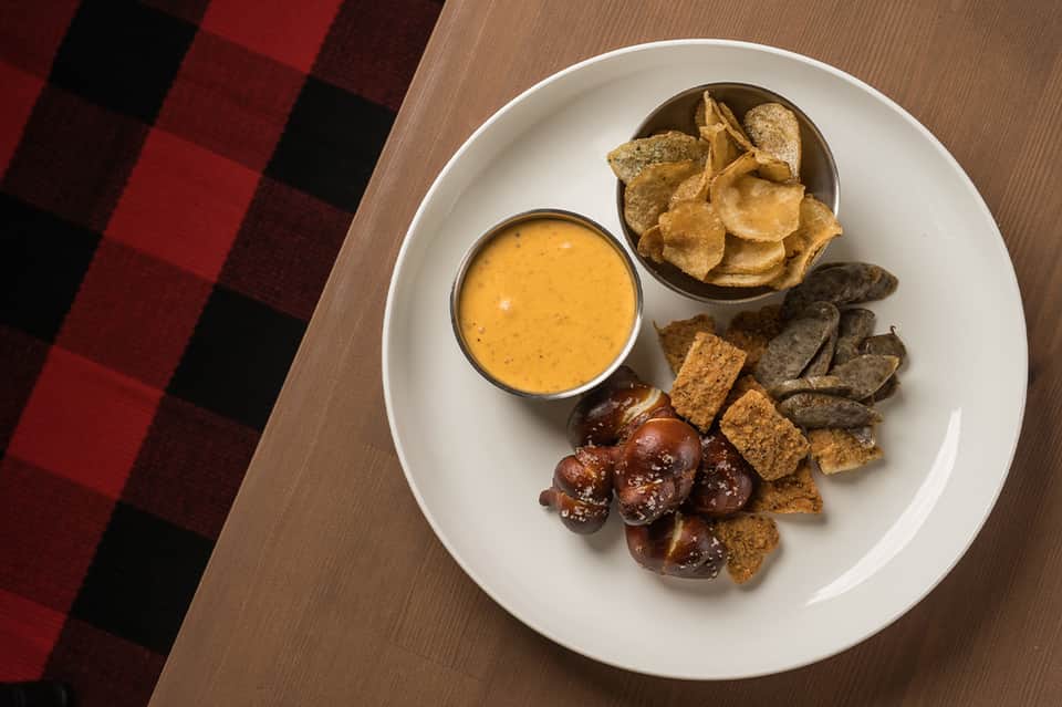 Appetizer platter with dip, tortilla chips, bread, and olives on white plate