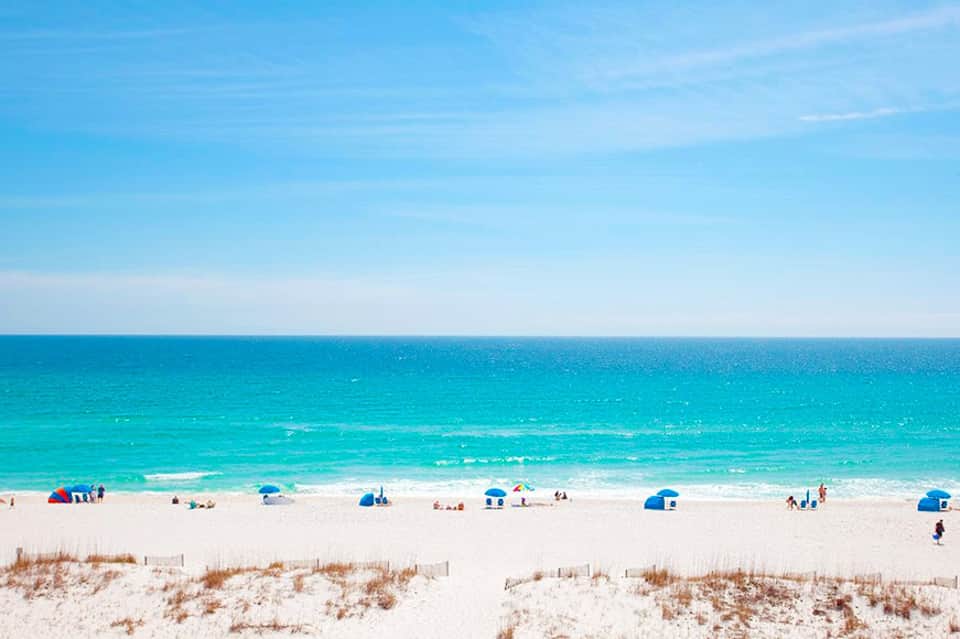 Pristine sandy beach with turquoise ocean, beach umbrellas, and clear blue sky
