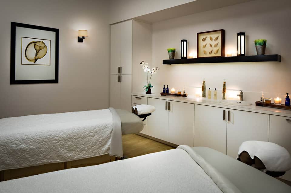 Modern spa treatment room with massage bed and white cabinetry with toiletries