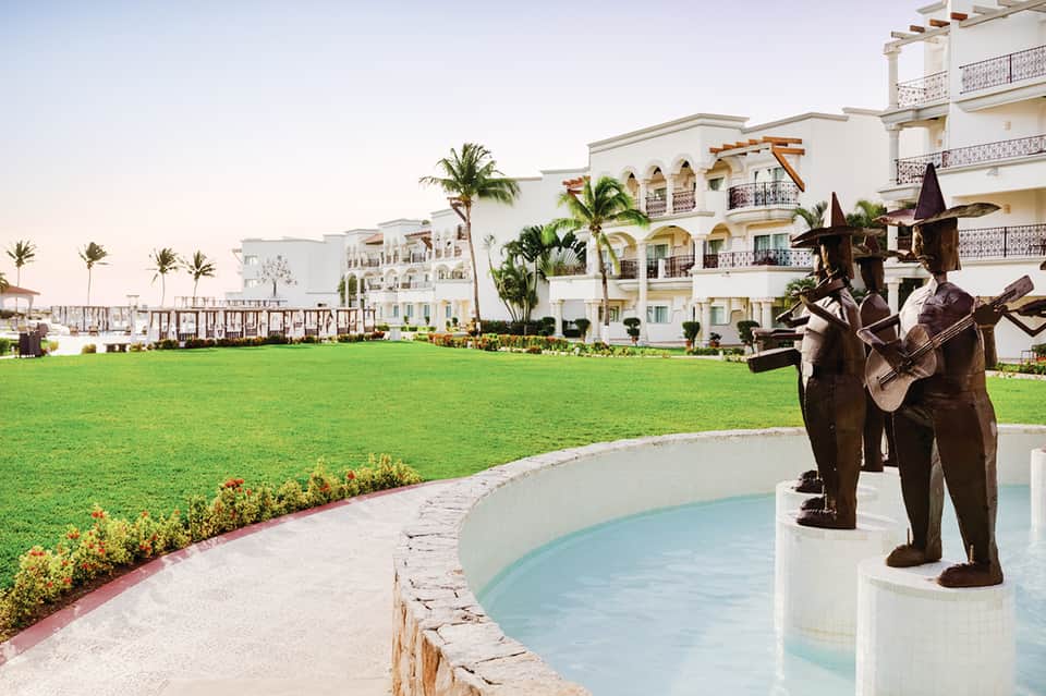 Beachfront resort grounds featuring sculptural art installation, manicured lawn, white building, and ocean view