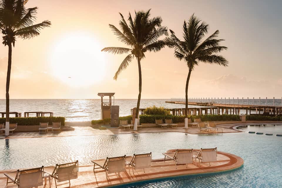 Waterfront resort pool at golden hour with palm trees and ocean pier
