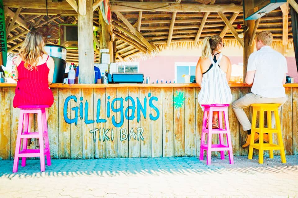 Colorful tiki bar on the beach with pink and yellow stools and blue signage