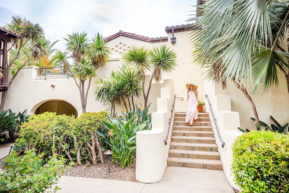 Spanish-style resort courtyard with white staircase, palm trees, and arched architectural details