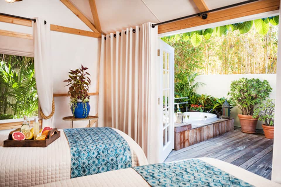 Beachfront bedroom with canopy bed, ocean views, wooden beams, and private patio access