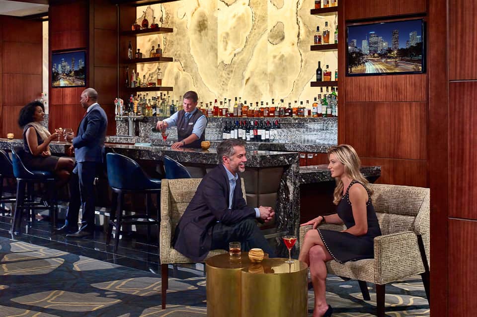 Upscale hotel bar lounge with wood paneling, marble countertop, and guests enjoying drinks