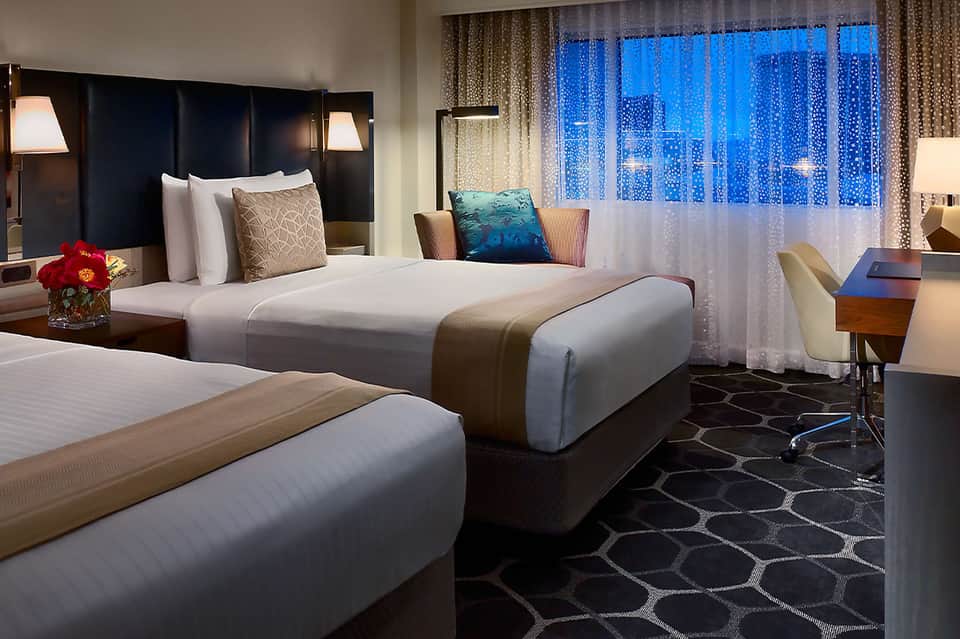 Upscale hotel room with two beds, dark headboards, and cityscape night view through large windows