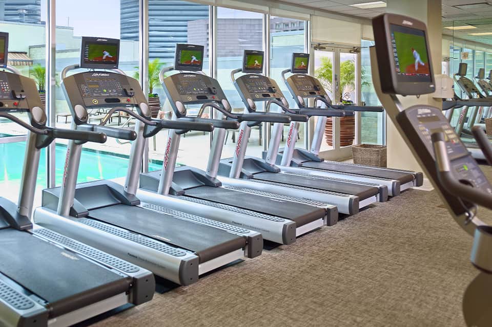 Hotel fitness center with treadmills, large windows overlooking pool and palm trees