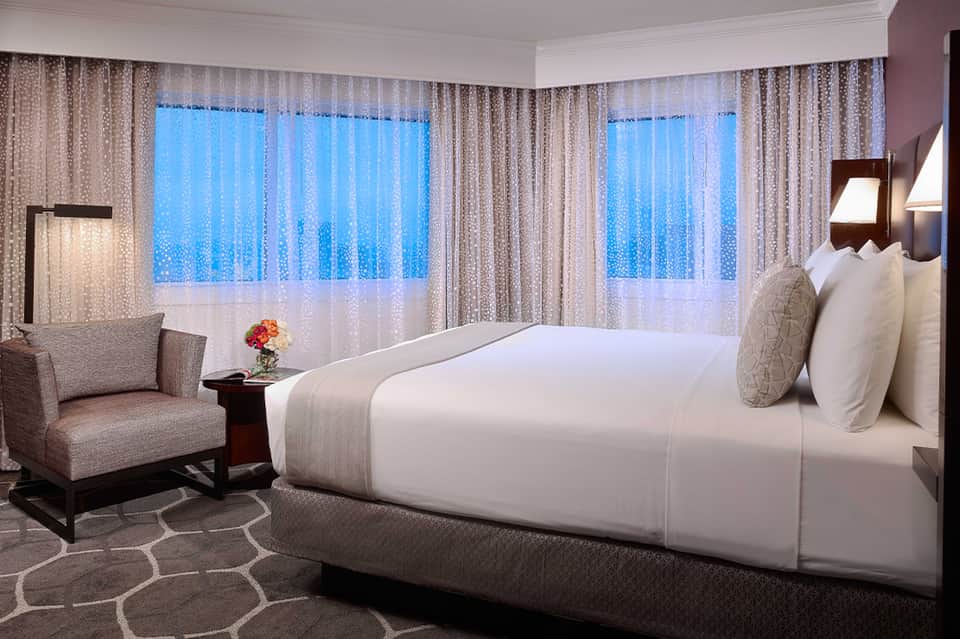 Luxury hotel room with white bedding, city view through floor-to-ceiling windows