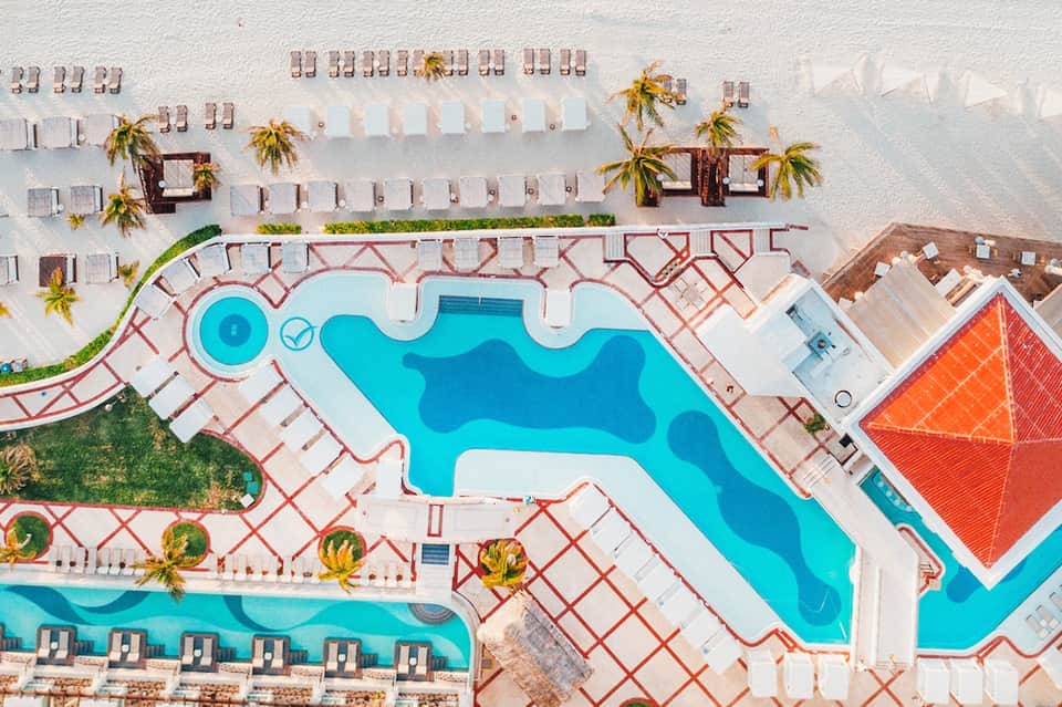 Aerial view of resort pool complex with decorative pavement patterns and organized beach loungers