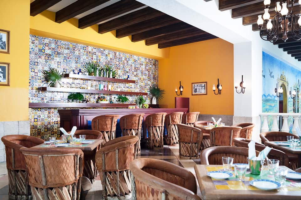 Vibrant restaurant dining area with colorful tile backsplash, orange walls, and leather seating