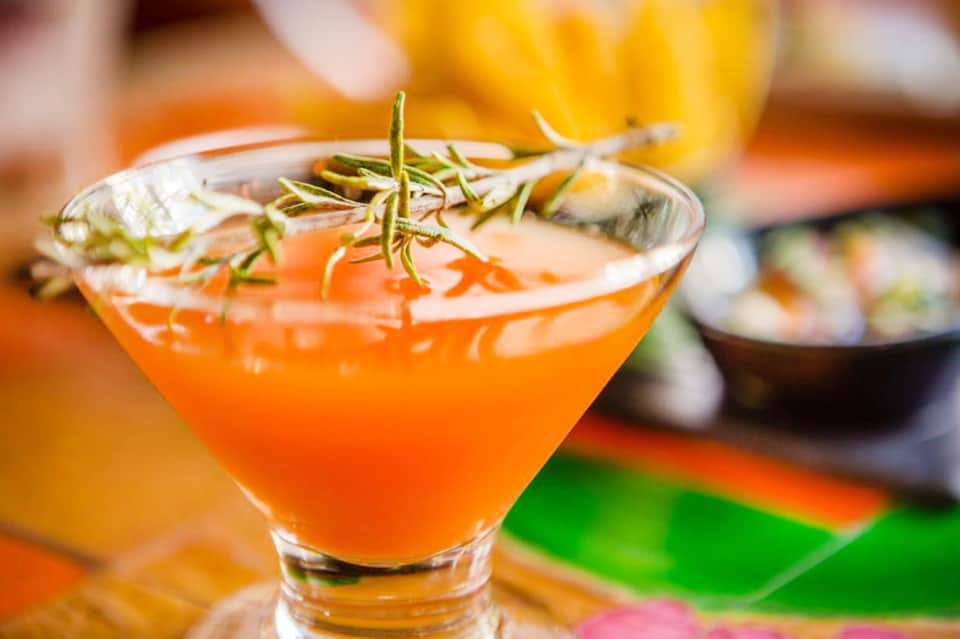 Colorful cocktail with orange juice, rosemary garnish, and ice in a martini glass