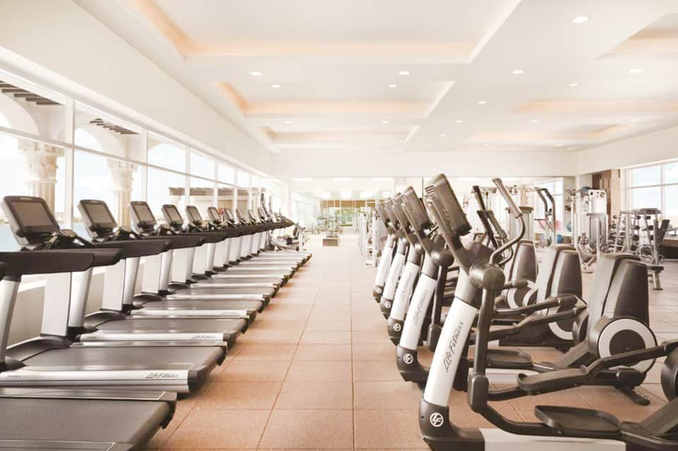 Modern hotel fitness center with rows of treadmills and exercise equipment under coffered ceiling