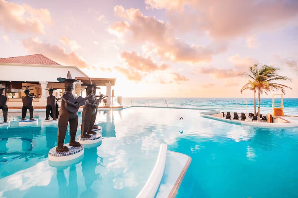 Infinity pool overlooking ocean with statues and sunset sky