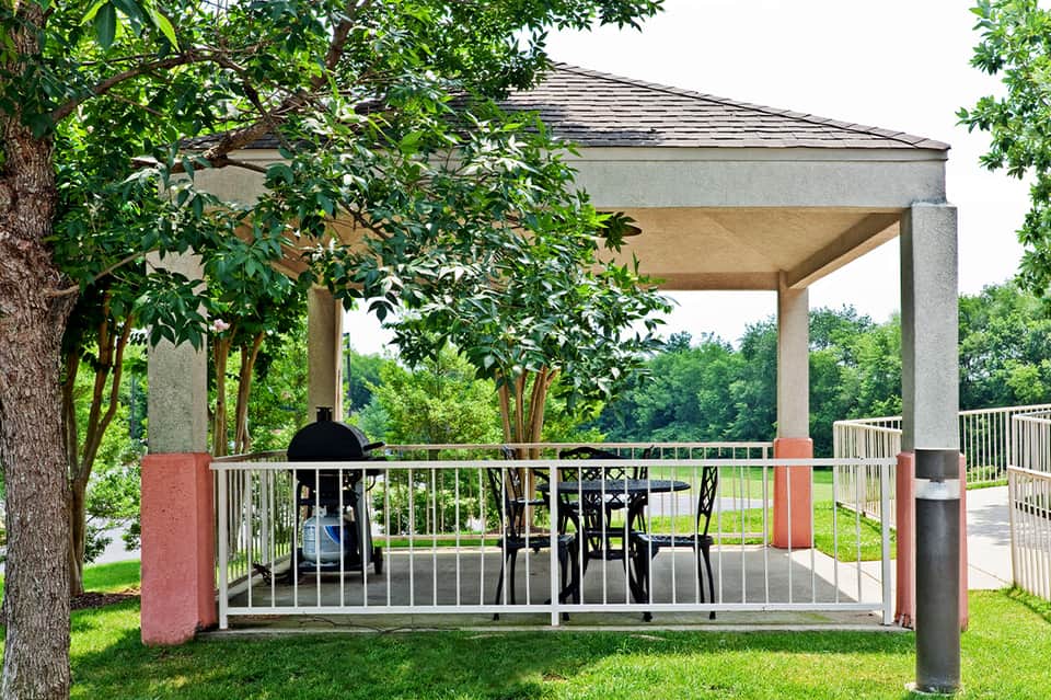 Covered outdoor pavilion with grilling station overlooking lush green lawn and landscaped grounds