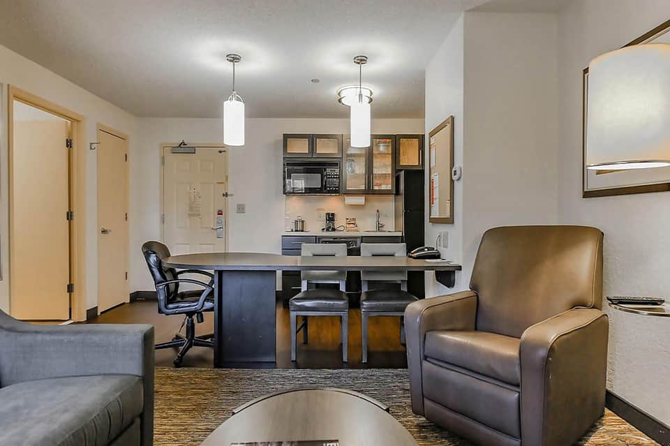 Modern hotel suite kitchenette with dark cabinetry, seating area, and contemporary furnishings