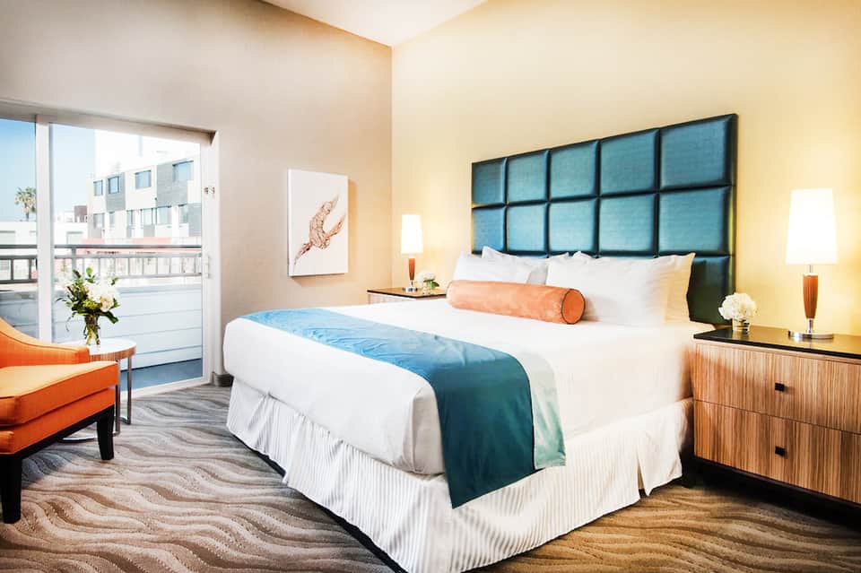 Contemporary hotel room with king bed, blue headboard, balcony, warm lighting