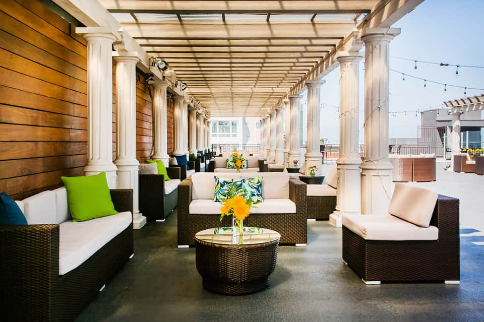 Rooftop lounge area with white pergola, rattan seating, and colorful accent pillows