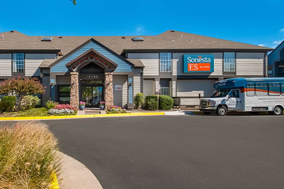 Sonesta ES Suites hotel exterior with stone entrance, professional signage, and shuttle vehicle