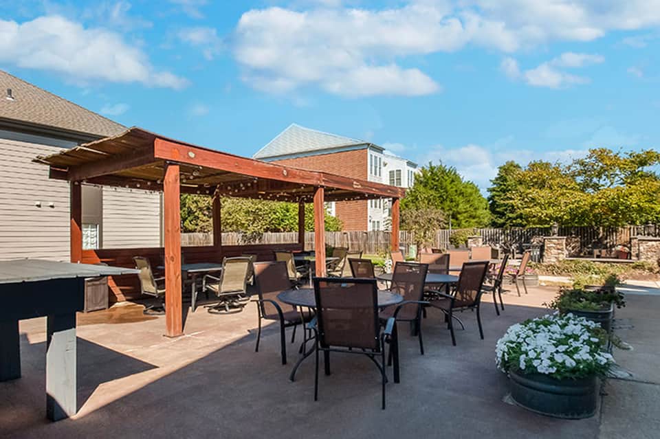 Wooden pergola patio with dining tables, lounge chairs, brick home, and landscaped grounds