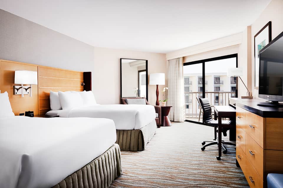 Spacious hotel room with two queen beds, desk, and balcony with city views