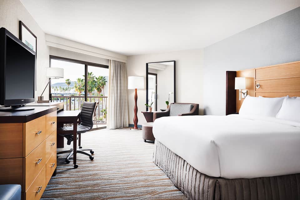 Modern hotel room with two beds, ocean-view balcony, wooden furniture, and contemporary décor