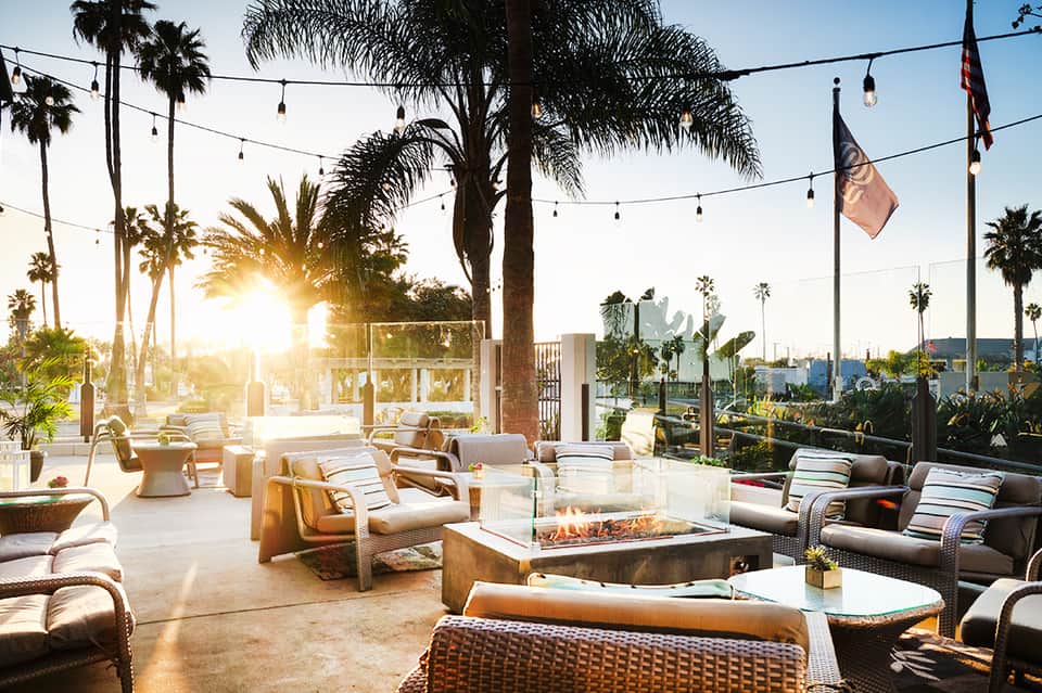 Modern resort patio at sunset with fire pit, lounge seating, and palm trees