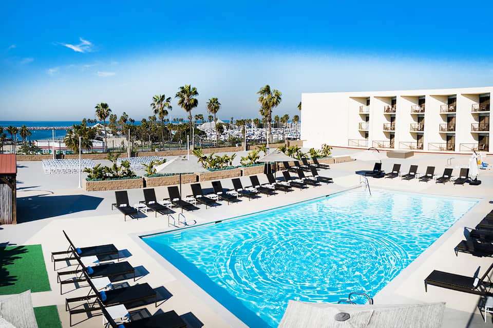 Contemporary beachfront pool with blue water, black loungers, ocean views, and hotel building facade