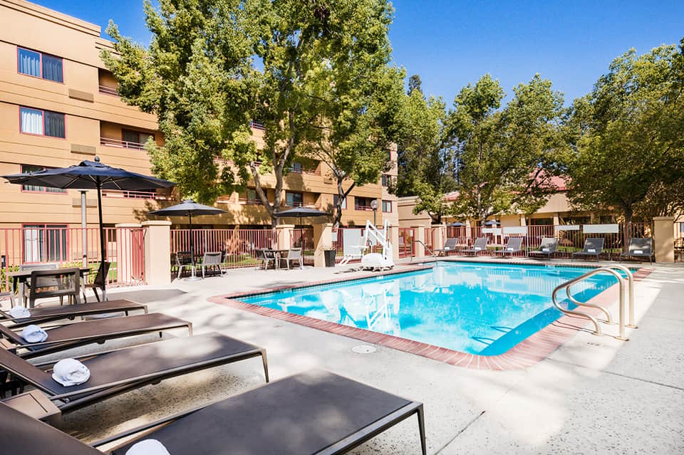 Resort pool with loungers, umbrellas, trees, and apartment buildings courtyard