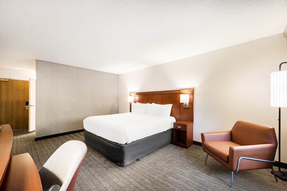 Hotel room with round bed, wood headboard, cognac leather chairs, and neutral tones