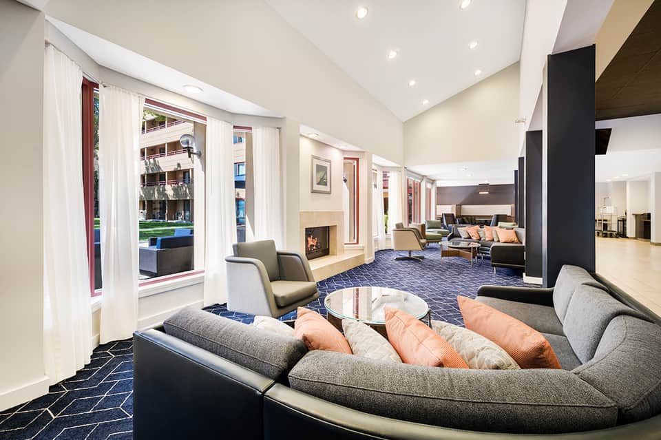 Contemporary hotel lobby lounge with curved seating, fireplace, and large windows
