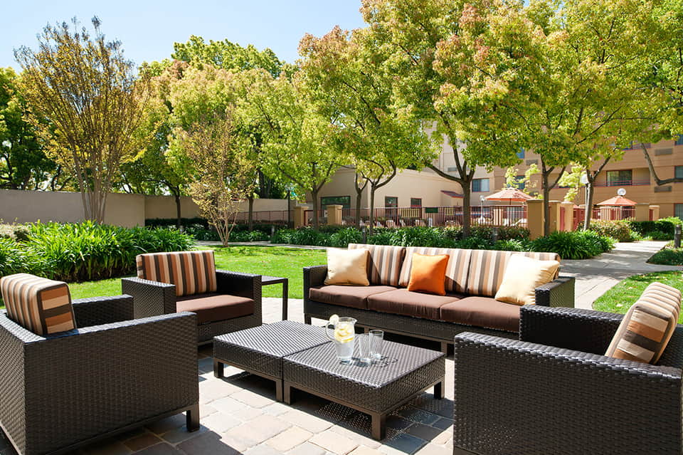 Outdoor courtyard lounge with rattan furniture, striped cushions, and mature trees