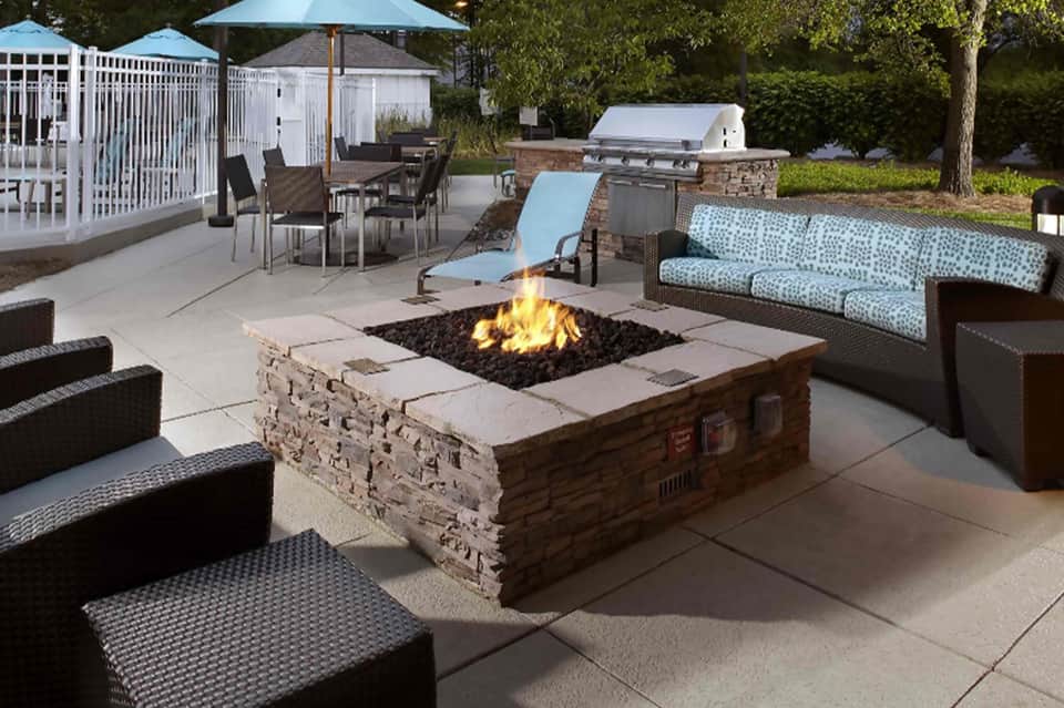 Backyard patio with fire pit, lounge seating, grill, and umbrella near white railing