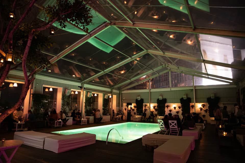 Evening poolside event under glass ceiling with green uplighting, lounge seating, and ambient lighting