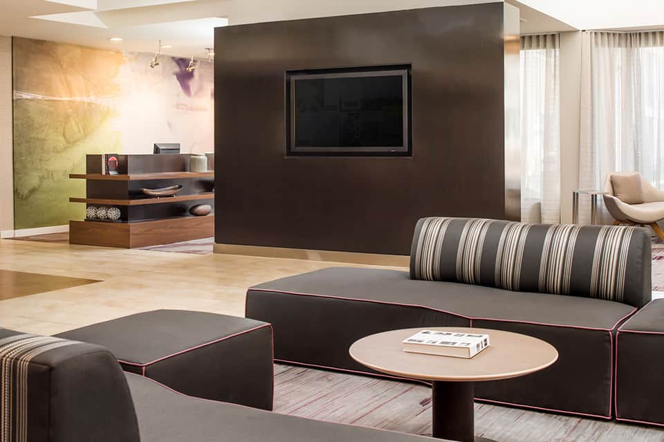 Modern hotel suite with dark accent wall, TV, striped sofa, low tables, and contemporary furnishings