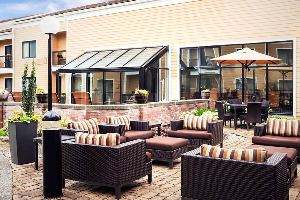 Outdoor patio with wicker lounge seating, striped cushions, umbrellas, and modern glass structure