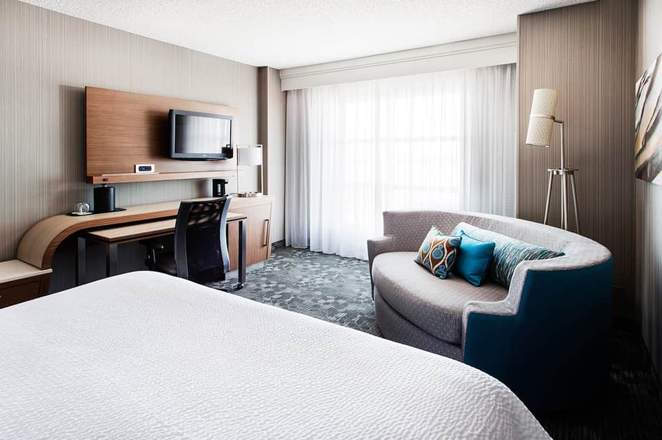 Spacious hotel room with king bed, work desk, sofa, and sliding glass doors to balcony